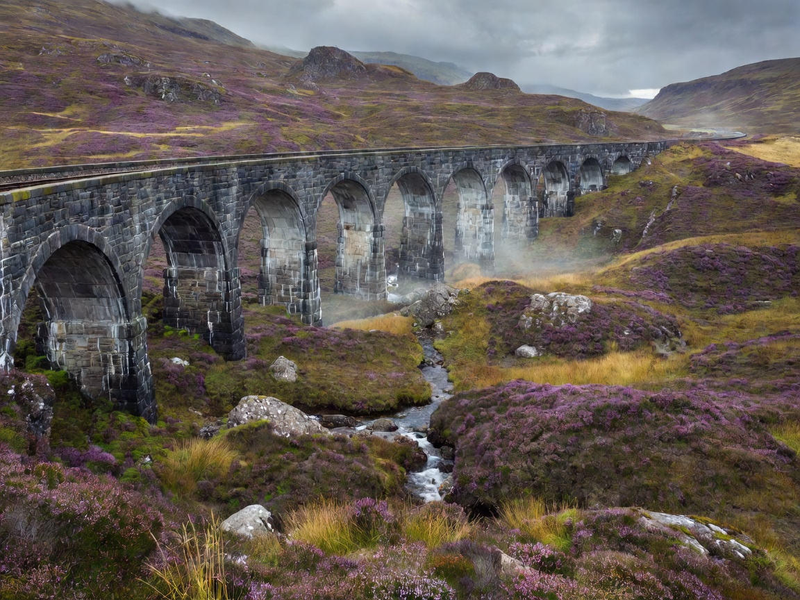 Curved stone railway viaduct crossing a wild heather valley in Scotland